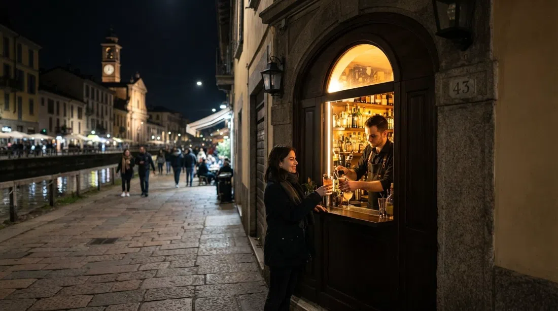 la pequeña ventanilla de Backdoor 43 en Ripa di Porta Ticinese de noche, con un interior de bar estrecho y una ventana de servicio de cócteles iluminada